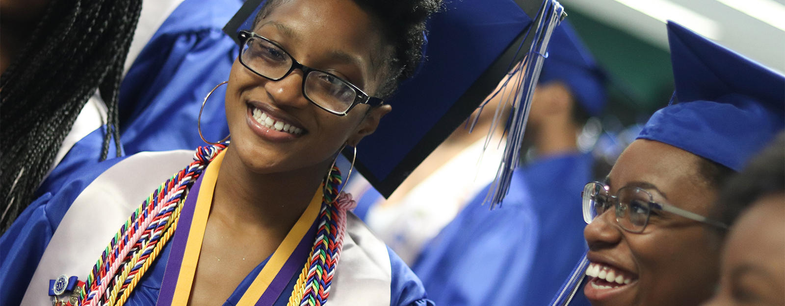 Student smiling at graduation with multiple academic cords on their robe.