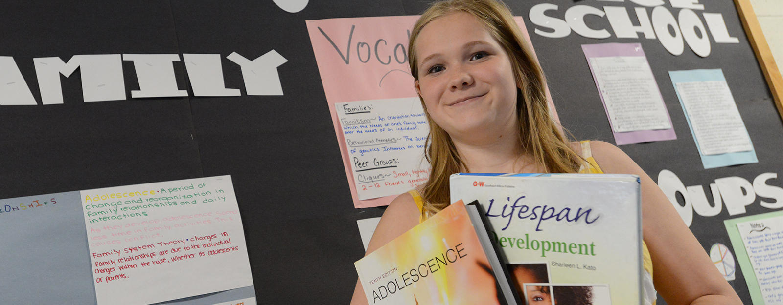Student holding an armful of FACS textbooks in front of a FACS bulletin board.