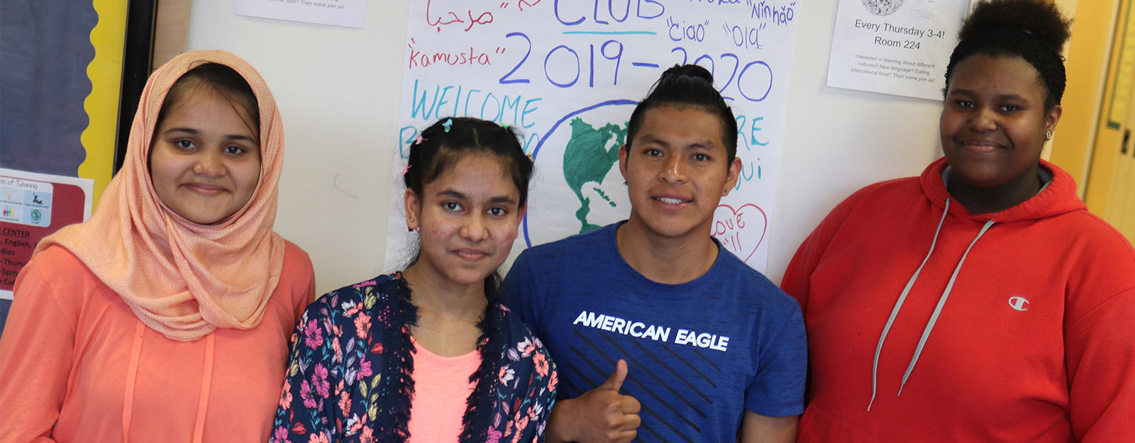 Students posing in front of a poster for international clubs.