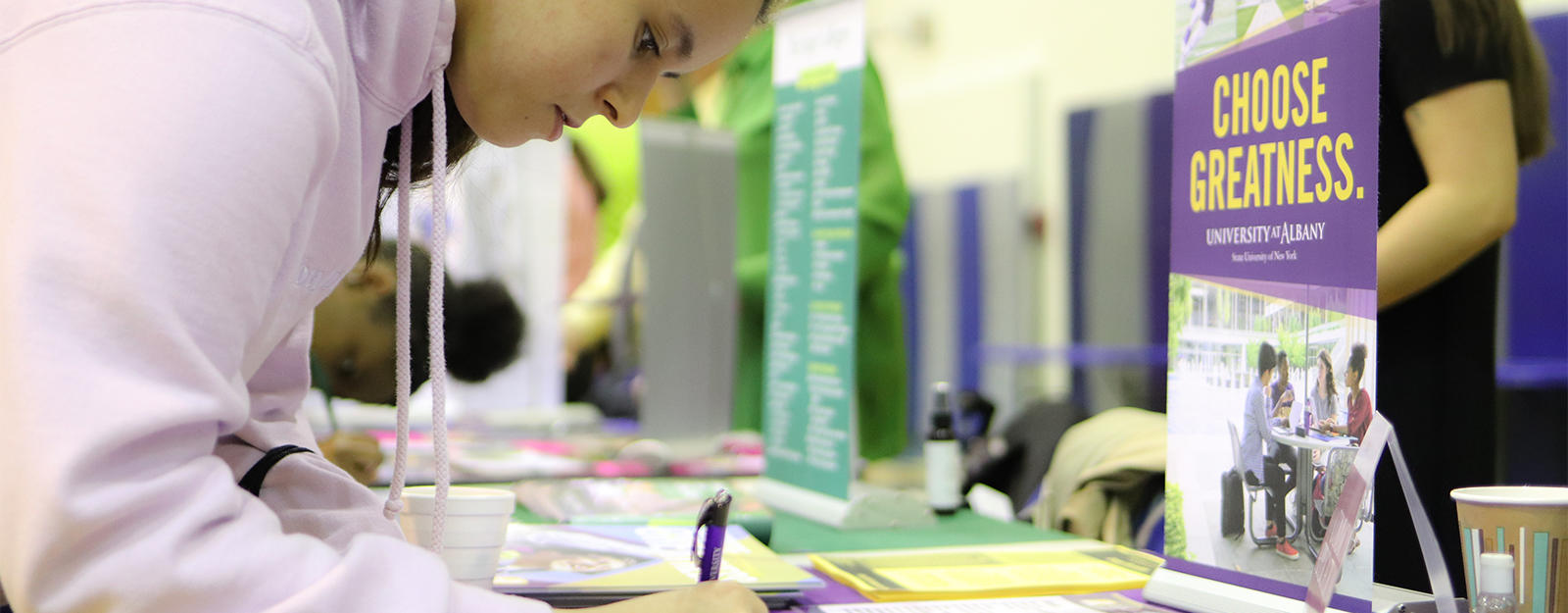 Student filling out paperwork at a SUNY Albany table during a college fair.