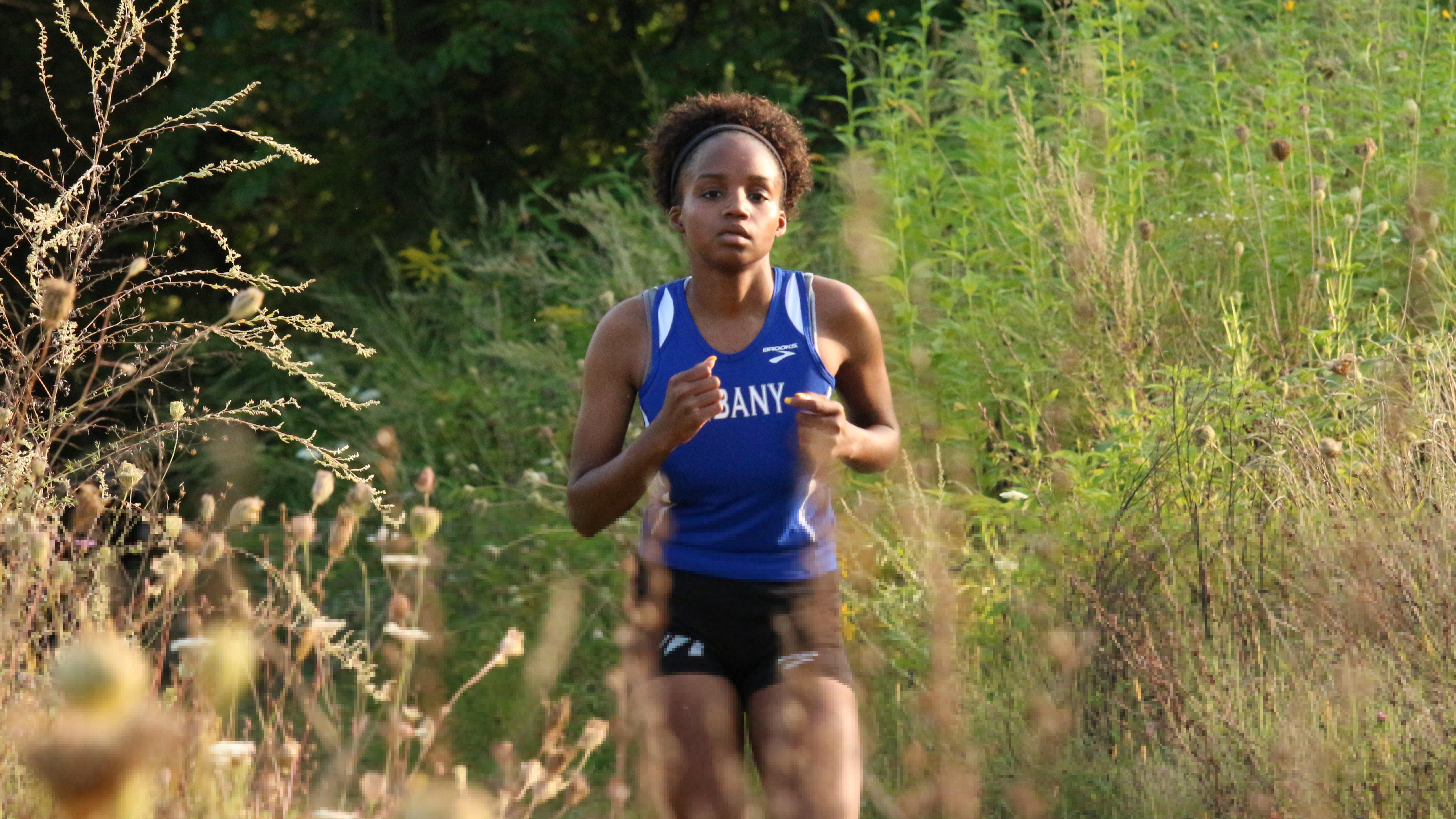 Female student running through the woods during a cross country track meet.