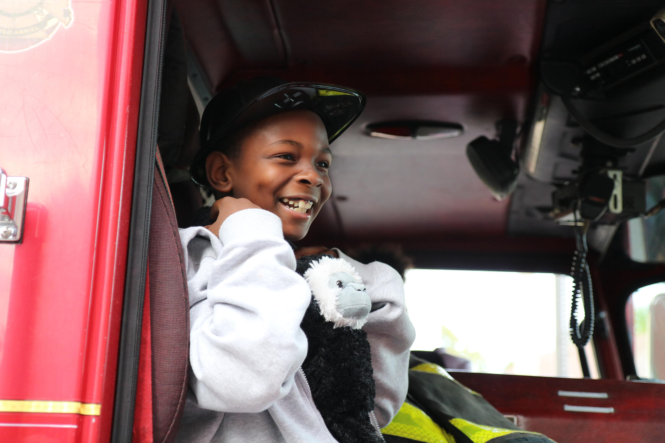 Student smiling while sitting in a firetruck wearing a firefighter's helmet