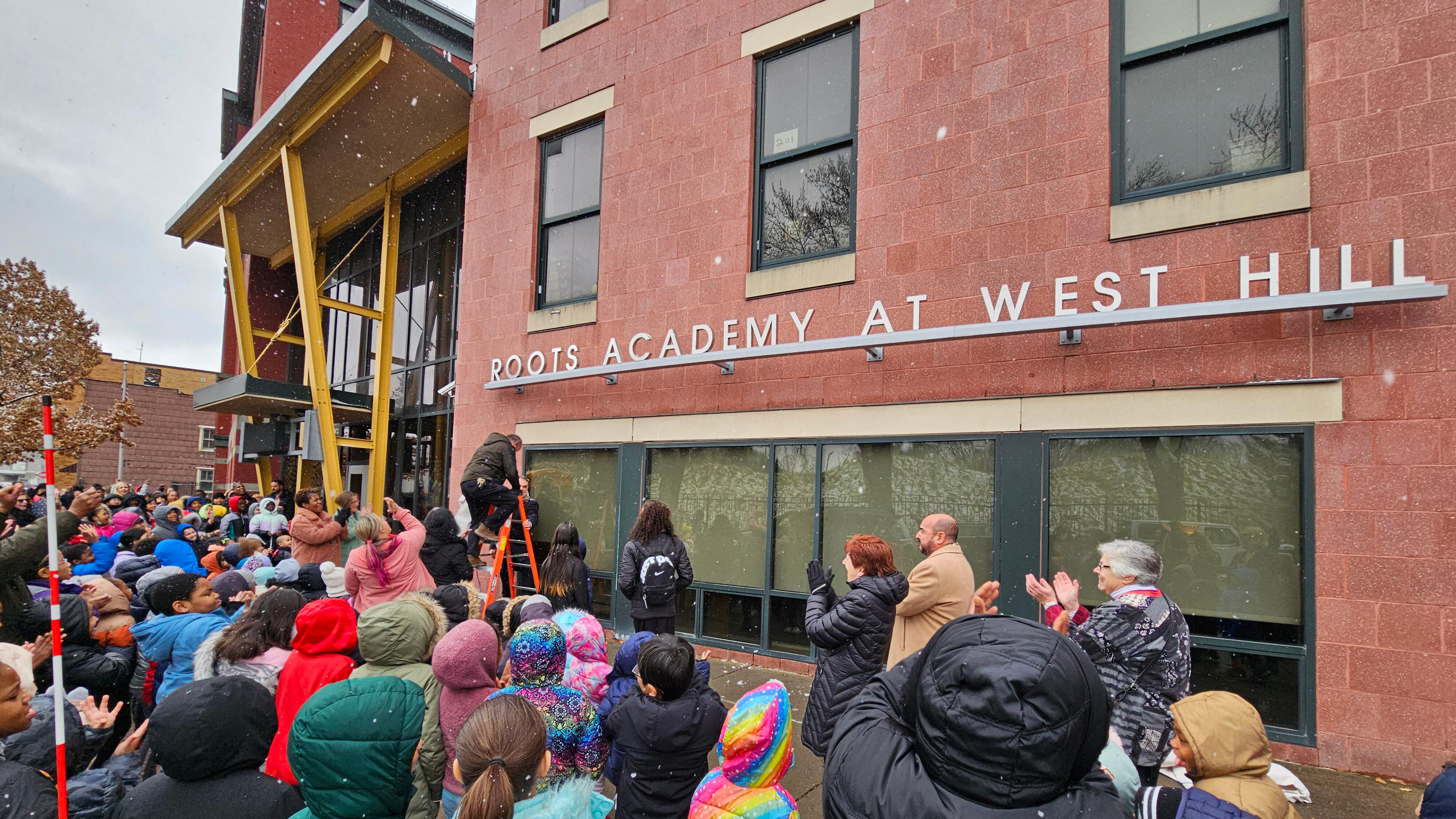 Community celebration in front of the new Roots Academy at West Hill sign