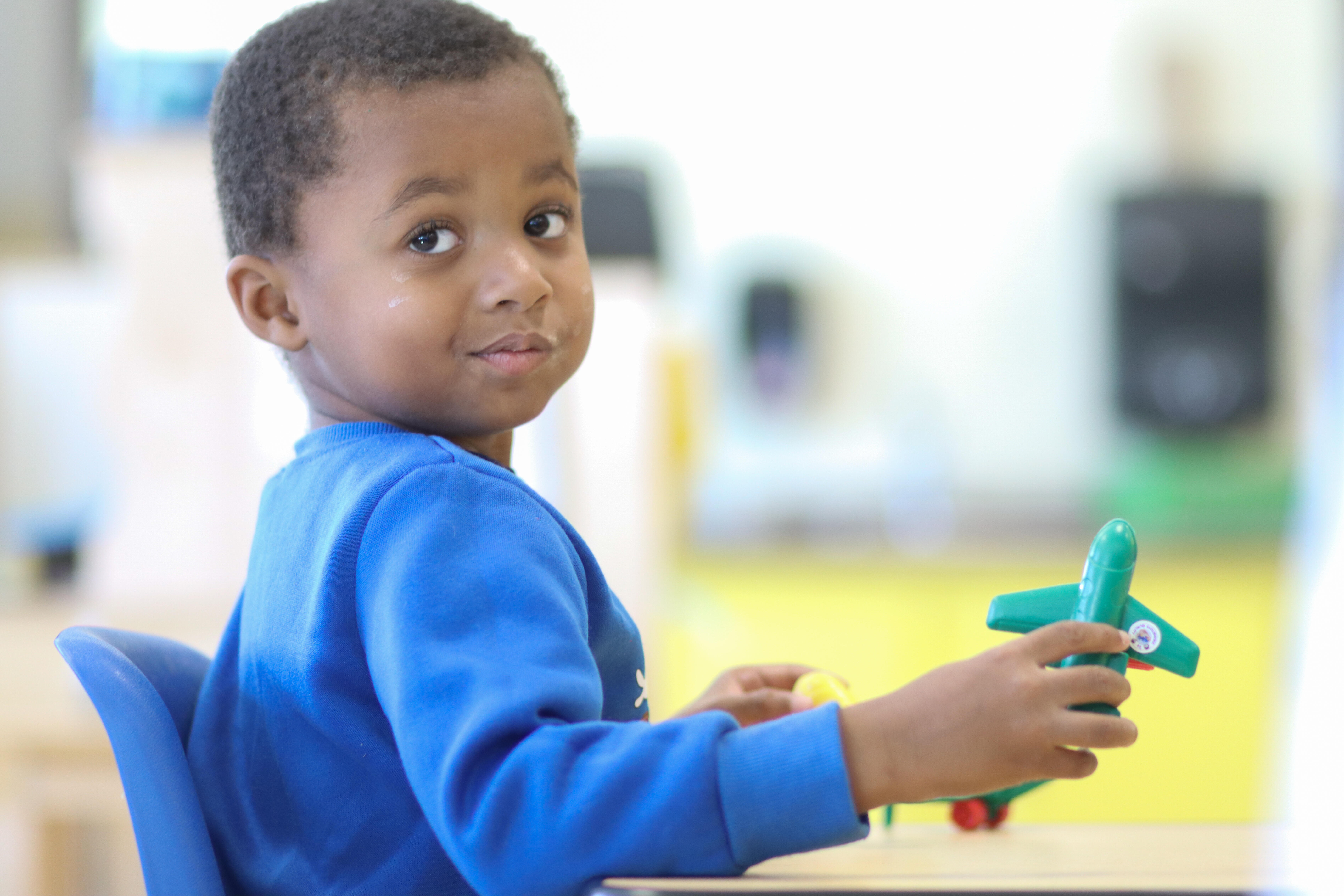 Pre-K student smiling while playing with a toy airplane
