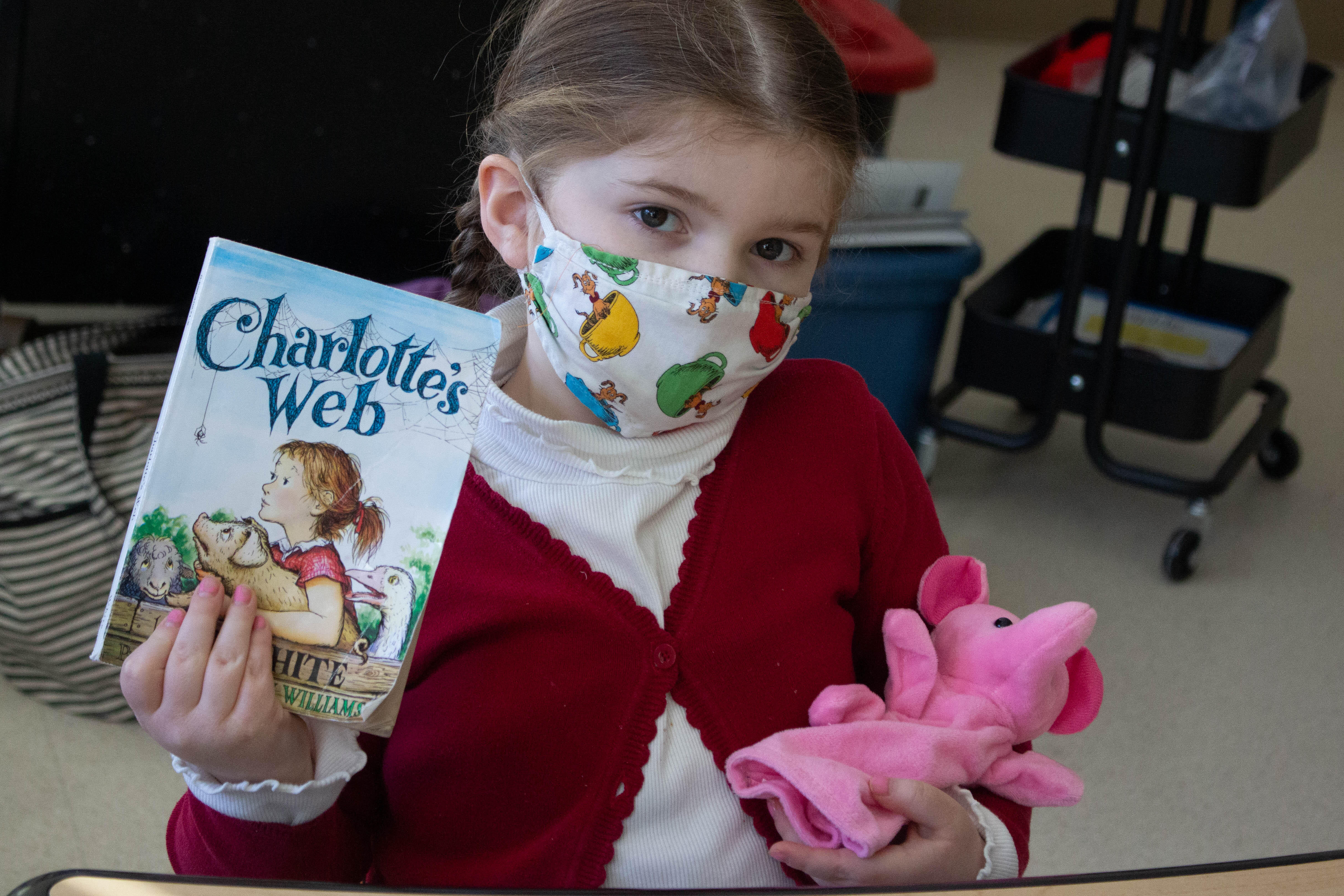 Student posing for a picture holding up a copy of Charlotte's Web and a toy pig