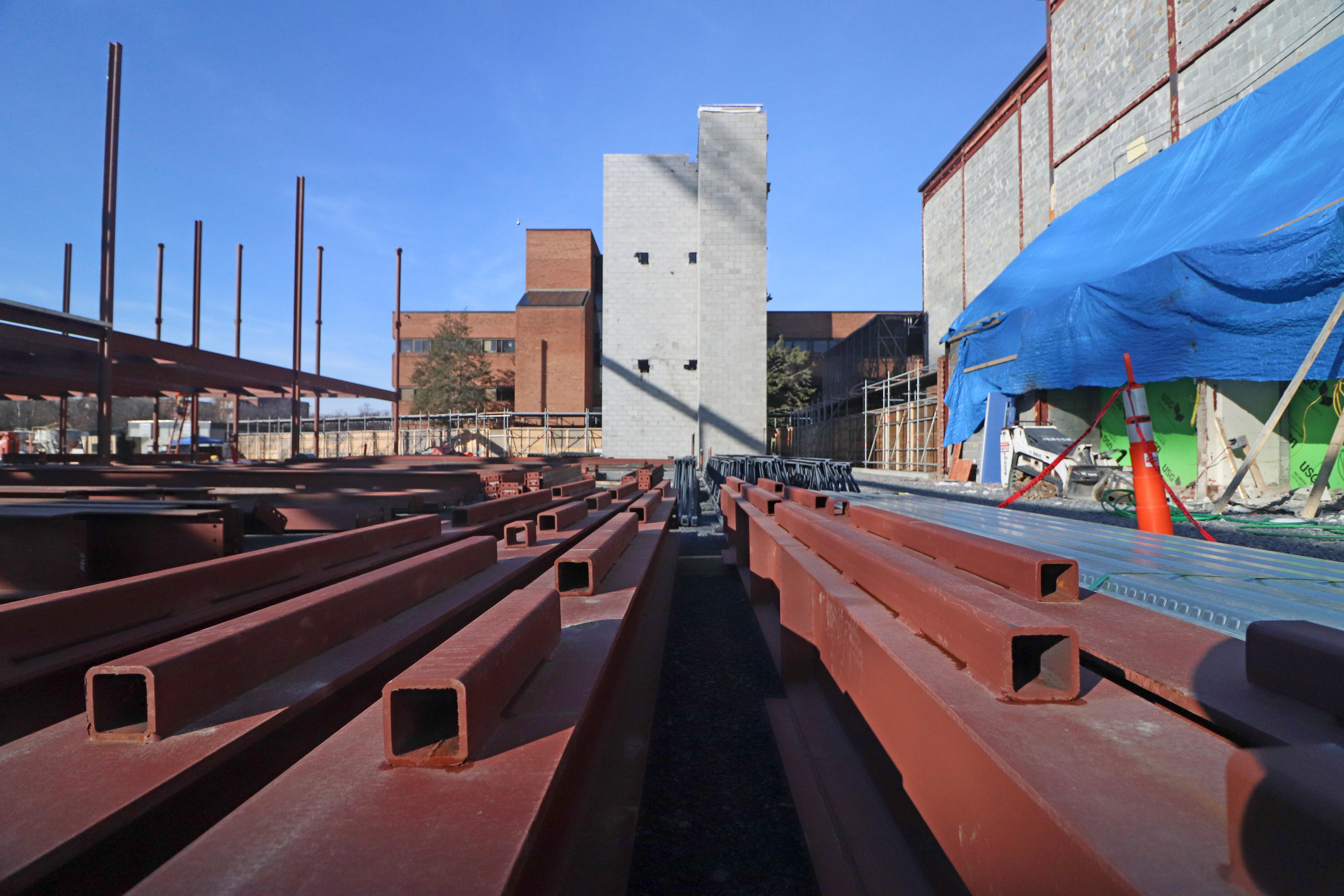 A view of the existing Albany High building as seen from the construction site, with the concrete stairwell of the new building visible among a stack of beams.