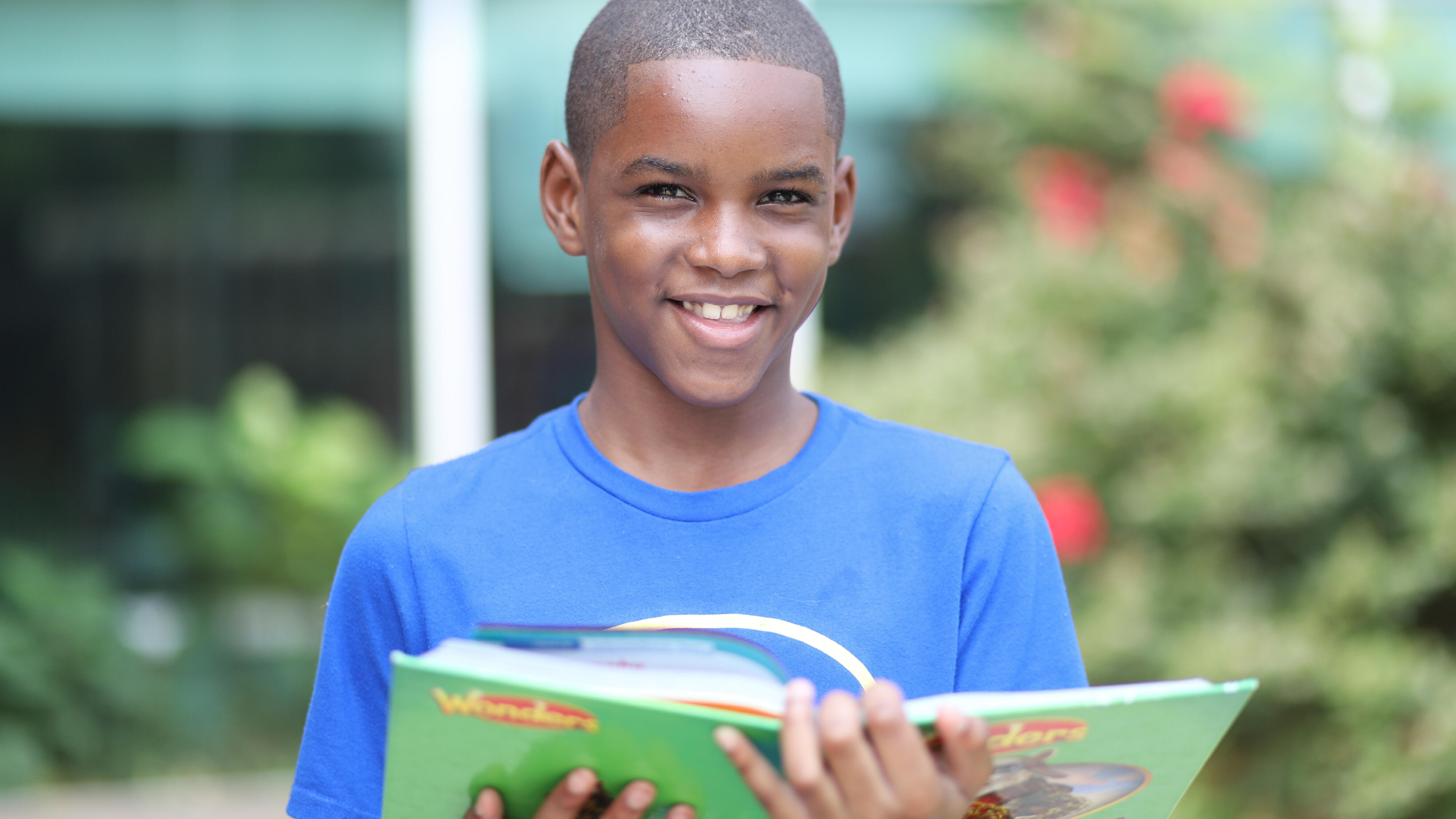 Student smiling while reading a textbook outside the school