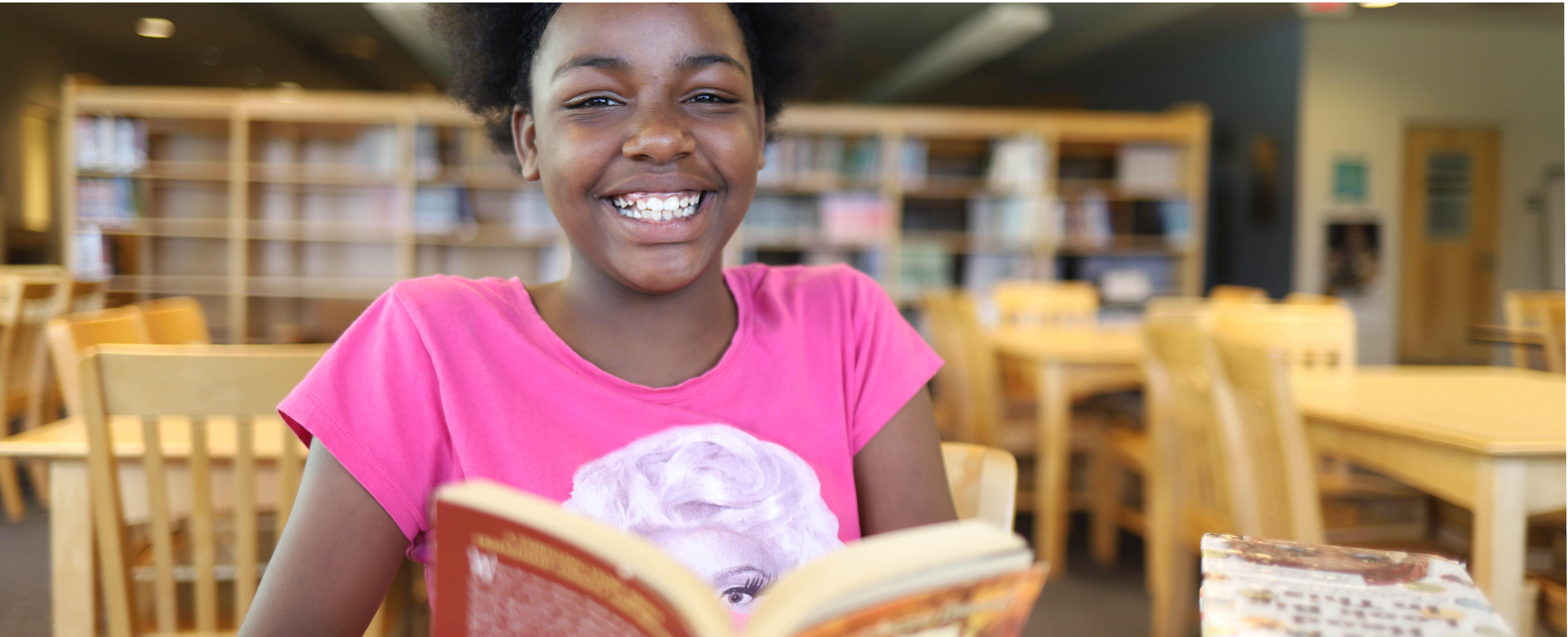Student smiling while reading a book in the library